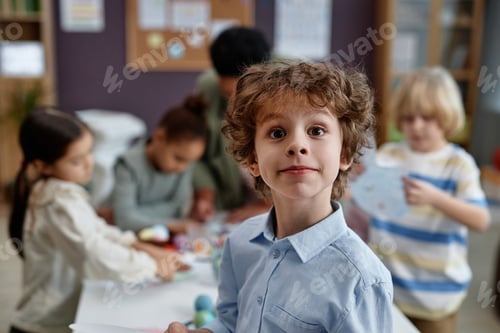 Preview: Cute curly haired boy looking at camera enjoying arts and crafts class