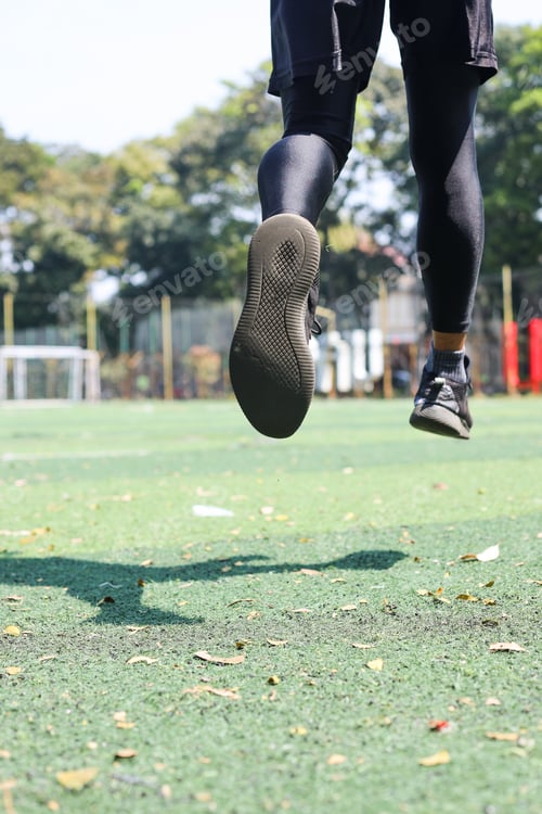 Preview: Back view of athletic runner man running on the grass, legs and shoes close up