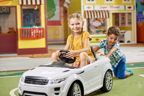 Preview: Boy pushing little girl in white car indoor.
