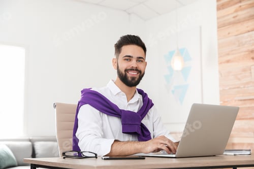 Preview: Handsome young man working with laptop at table in home office