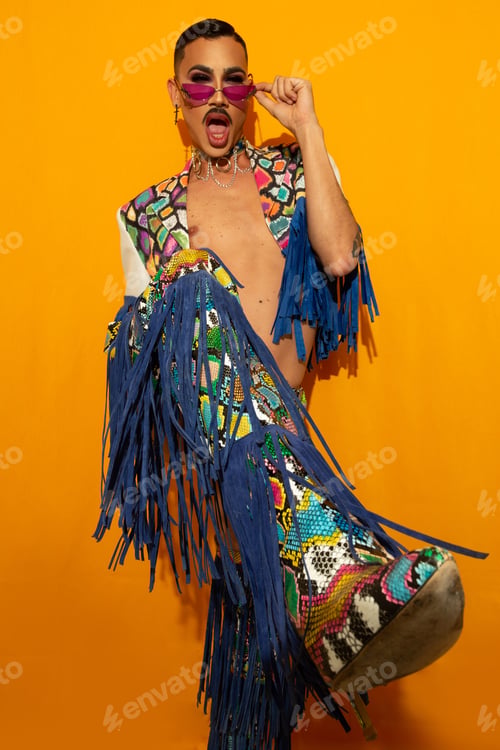 Preview: Portrait of a happy young drag queen smiling in a colorful dress on a yellow background.