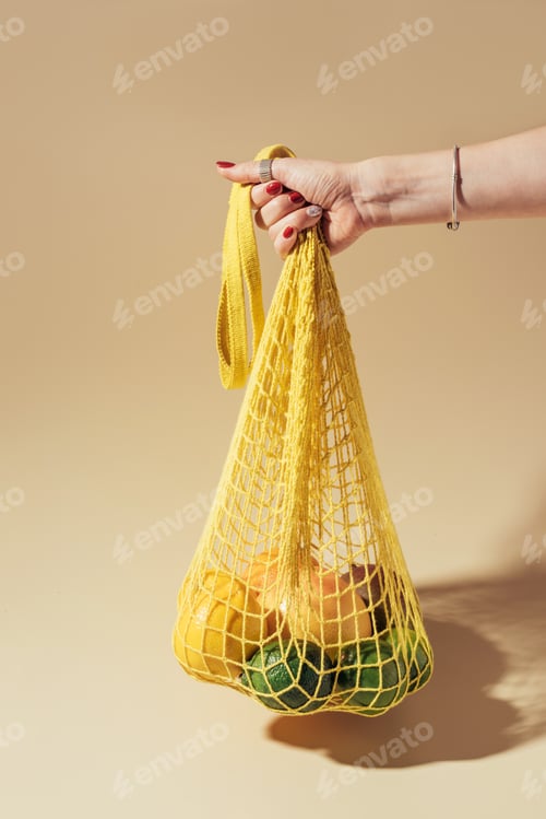 Preview: partial view of person holding string bag with fresh tropical fruits on brown
