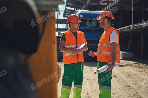Preview: Two Workers In Helmets Standing Near The Construction Site And Communicating