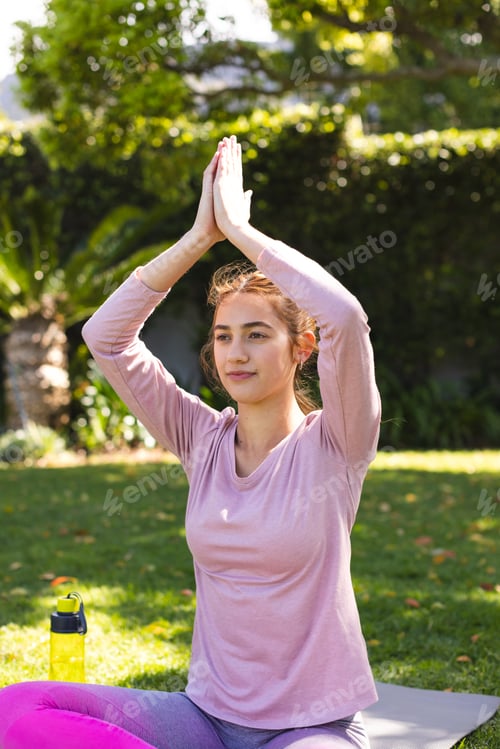 Preview: Happy biracial woman practicing yoga meditation sitting in sunny garden