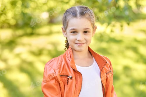 Preview: Caucasian female child smiling in orange jacket outdoors with green leafy