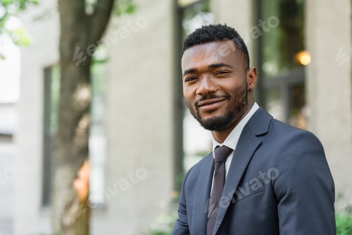 Preview: smiling african american businessman in suit looking at camera outside