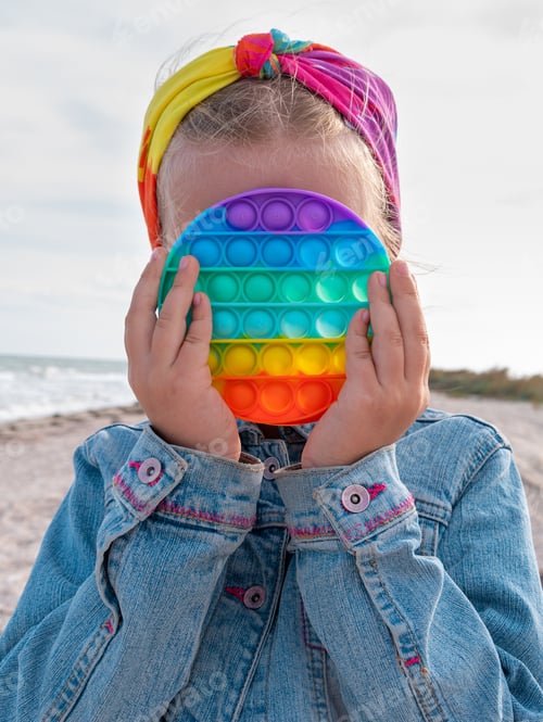 Preview: Blond child girl rainbow toy walking having fun on beach Bright colorful trendy antistress push toy