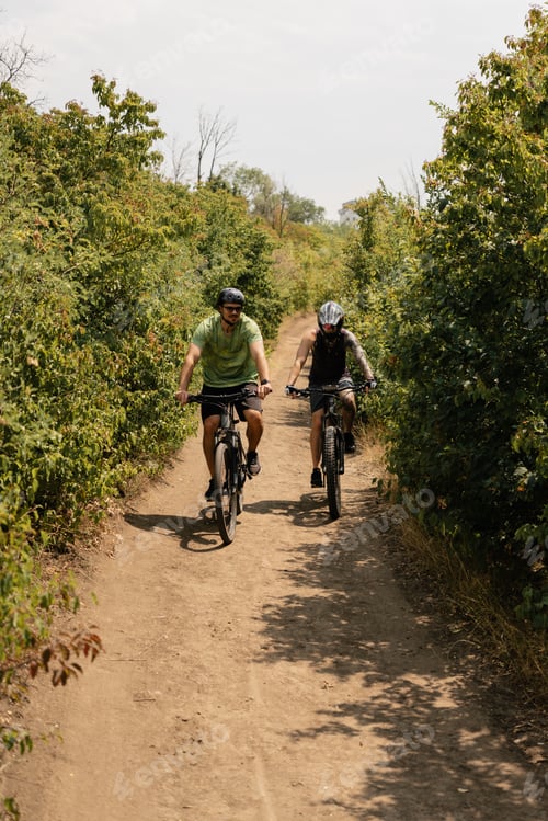 Preview: Two individuals biking on a dirt path through lush greenery and trees