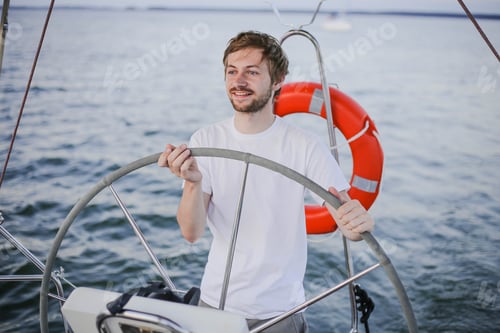 Preview: Happy young man steering wheel and looking far away on yacht on the sea. Sailing