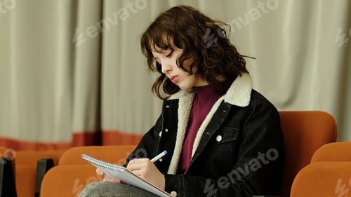 Preview: A girl pens her thoughts in a notebook while seated in a serene indoor space. The photo emphasizes