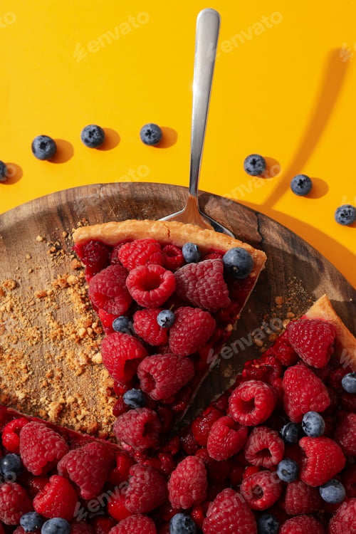 Preview: Pie with raspberries and blueberries on wooden plate on yellow background, top view