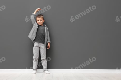 Preview: Little boy measuring his height near grey wall. Space for text