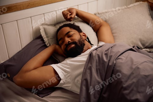 Preview: Smiling black man stretching in bed in the morning.