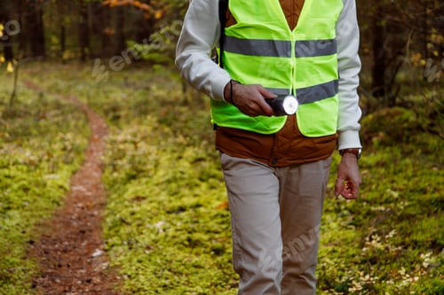 Preview: Male Volunteer of the Search and Rescue Team Dressed in Signal Vest with Flashlight in the Forest.