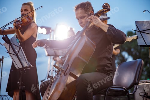 Preview: Male violoncellist playing in orchestra at outdoor concert