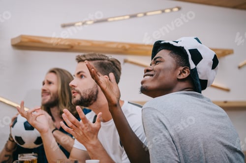 Preview: side view of multicultural group of male football fans gesturing by hands and watching soccer match