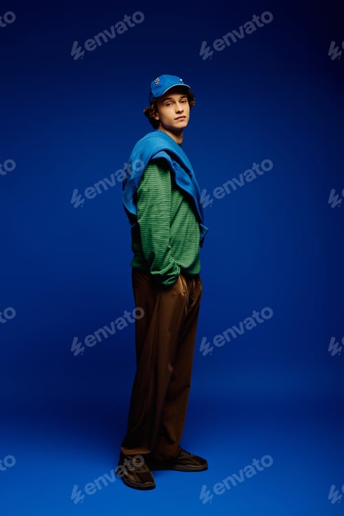 Preview: Young man showcases modern fashion and style against a vibrant blue background in a playful pose