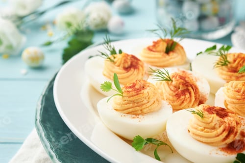Preview: Stuffed or deviled eggs with paprika and parsley on blue plate for easter table. Traditional dish fo