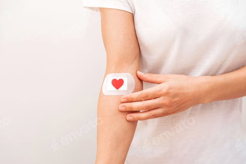 Preview: Person Touching a Bandage with Red Heart on Arm After Medical Procedure on grey background