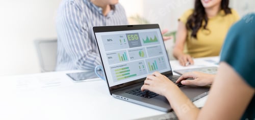 Preview: A professional is presenting business data during a meeting while a colleague types on a laptop