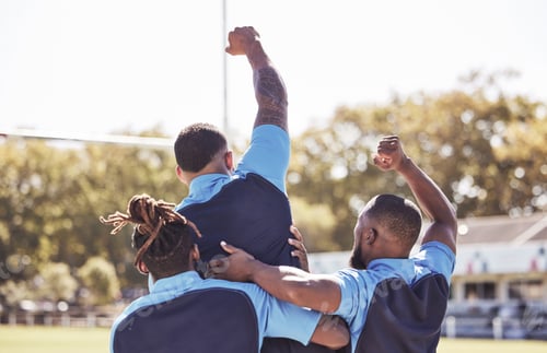 Preview: Diverse rugby teammates celebrating scoring a try or winning a match outside on a sports field. Rug