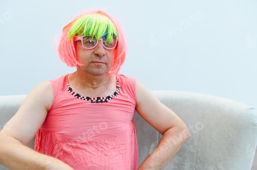 Preview: Man wearing colorful wig and pink dress sitting on sofa