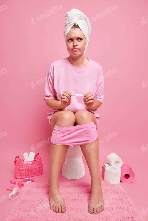 Preview: Vertical shot of displeased thoughtful woman holds pregnancy test dissatisfied with result dressed i
