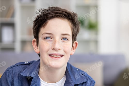Preview: Portrait of happy brunette teenage guy in braces sitting in bright room, smiling and looking at