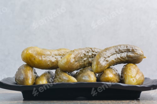 Preview: A dark plate full of delicious pickled cucumbers on white background