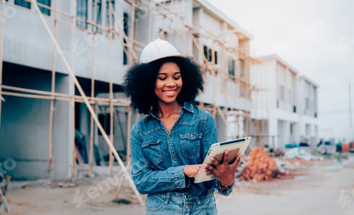Preview: portrait of young female architect wearing hardhat smiling happily looking at camera.
