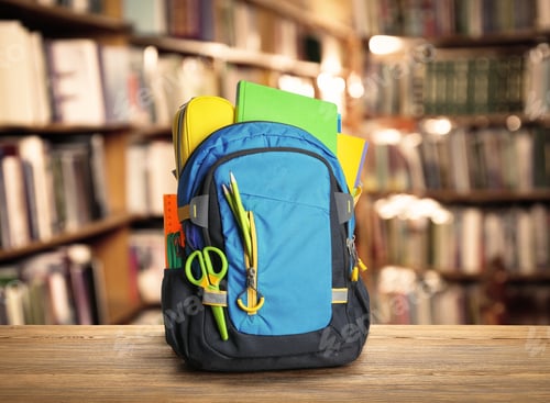 Preview: Backpack with school stationery on wooden table in library