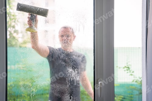 Preview: Young man cleans the windows in the house. He splashes detergent, rubs and removes water at the