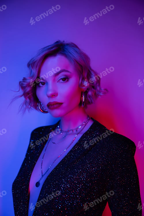 Preview: young woman with blonde curly hair posing in black tight dress on purple with pink light