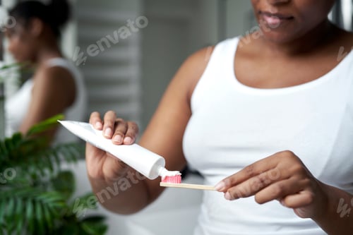 Preview: Detail of young African-American woman applying toothpaste on the wooden toothbrush