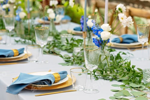 Preview: Banquet wedding table setting with blue napkins, gold cutlery, crystal, fresh flowers and candles.