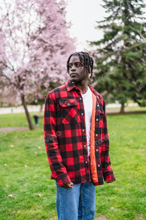 Preview: Young man wearing red and black lumberjack shirt standing in park