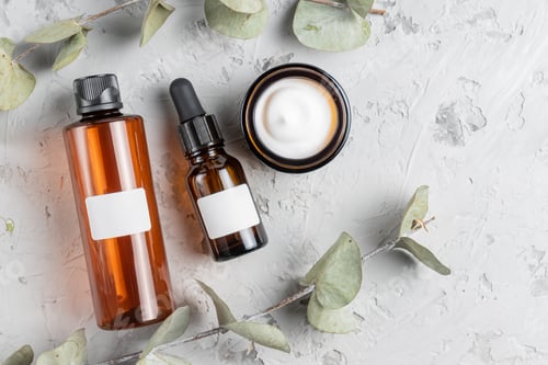 Preview: Cosmetic glass bottles with cream, toner and face mask on concrete background with dry eucalyptus