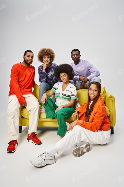 Preview: jolly african american community in bright casual wear sitting together on yellow couch on grey