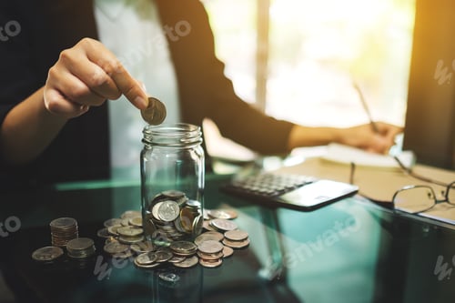 Preview: a businesswoman calculating, stacking and putting coins in a glass jar for saving money