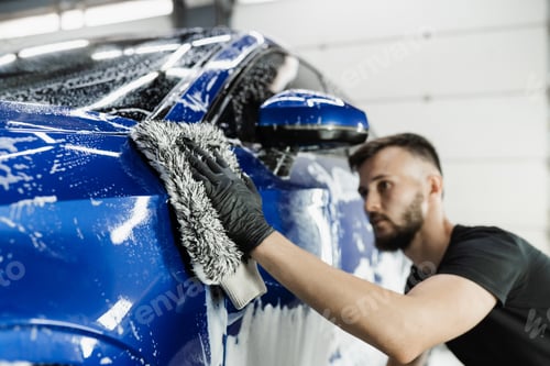 Preview: Hand washing car body with foam and microfiber glove in detailing service garage
