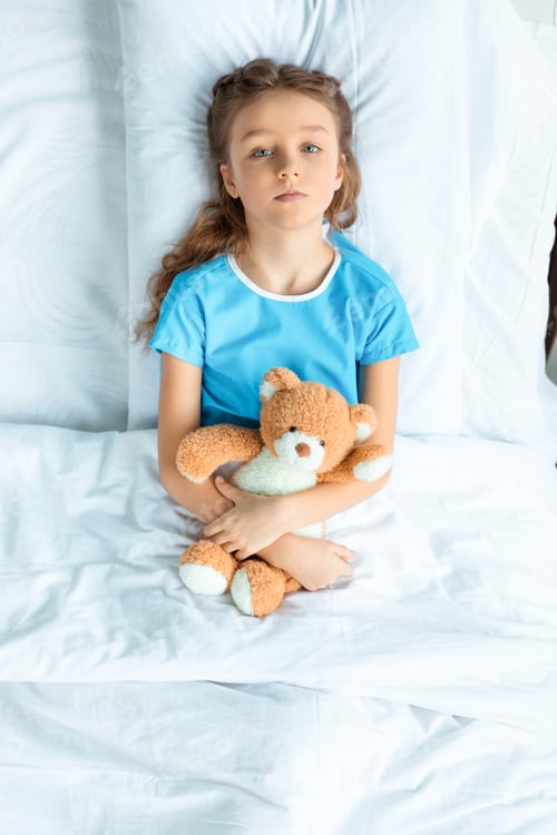Preview: top view of little patient with teddy bear lying on bed in hospital