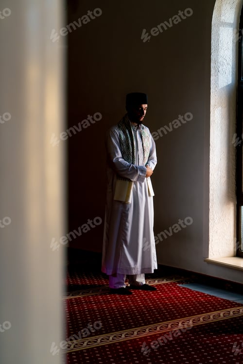 Preview: A Muslim believer in national clothes prays in the twilight by the window in the mosque kneels
