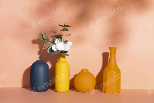 Preview: Beautiful white rose in a decorative yellow vase with empty vases against an orange wall