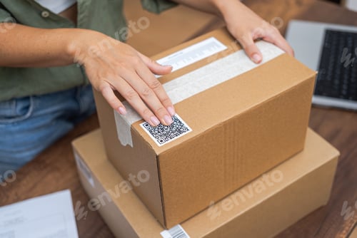 Preview: Woman post office worker works sticking barcode on cardboard box for sending goods to recipient