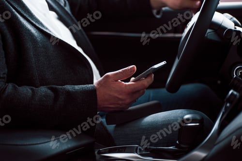 Preview: Working in the car using silver colored smartphone. Senior businessman