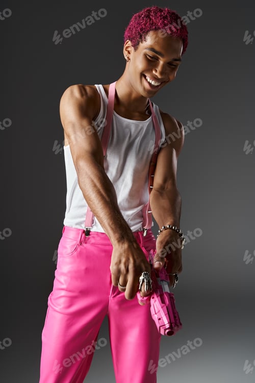 Preview: happy smiley man with pink hair in vibrant stylish attire with pink toy gun on gray background