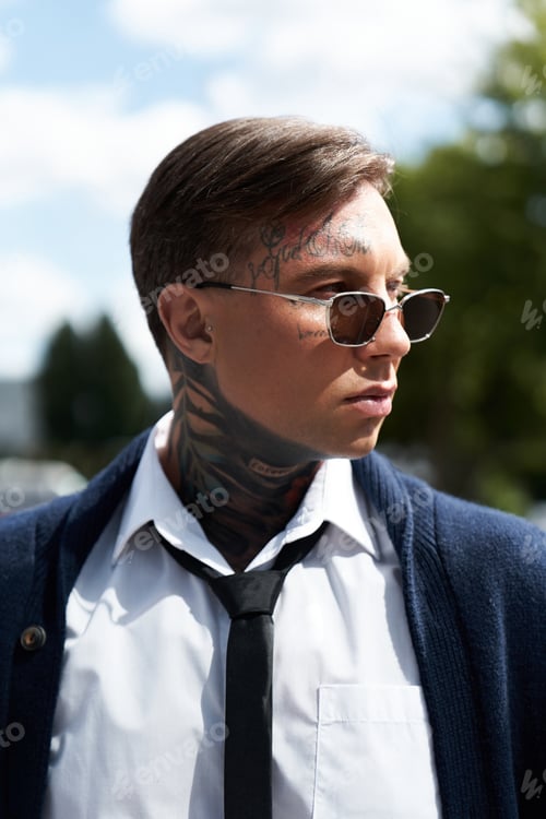 Preview: A confident young man with tattoos wears sunglasses and stylish casual attire under sunlight