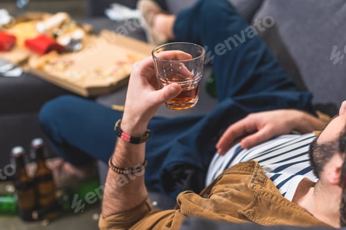 Preview: cropped image loner lying on sofa with glass of whiskey at living room