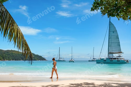 Preview: Adult woman walking on sandy tropical beach. Luxurious yachts moored in bay of turquoise sea