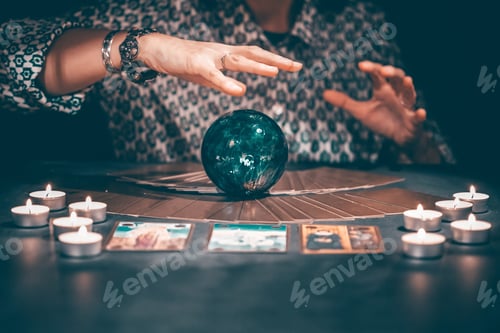 Preview: Tarot reader with tarot cards.Tarot cards face down on table near burning candles and crystal ball.